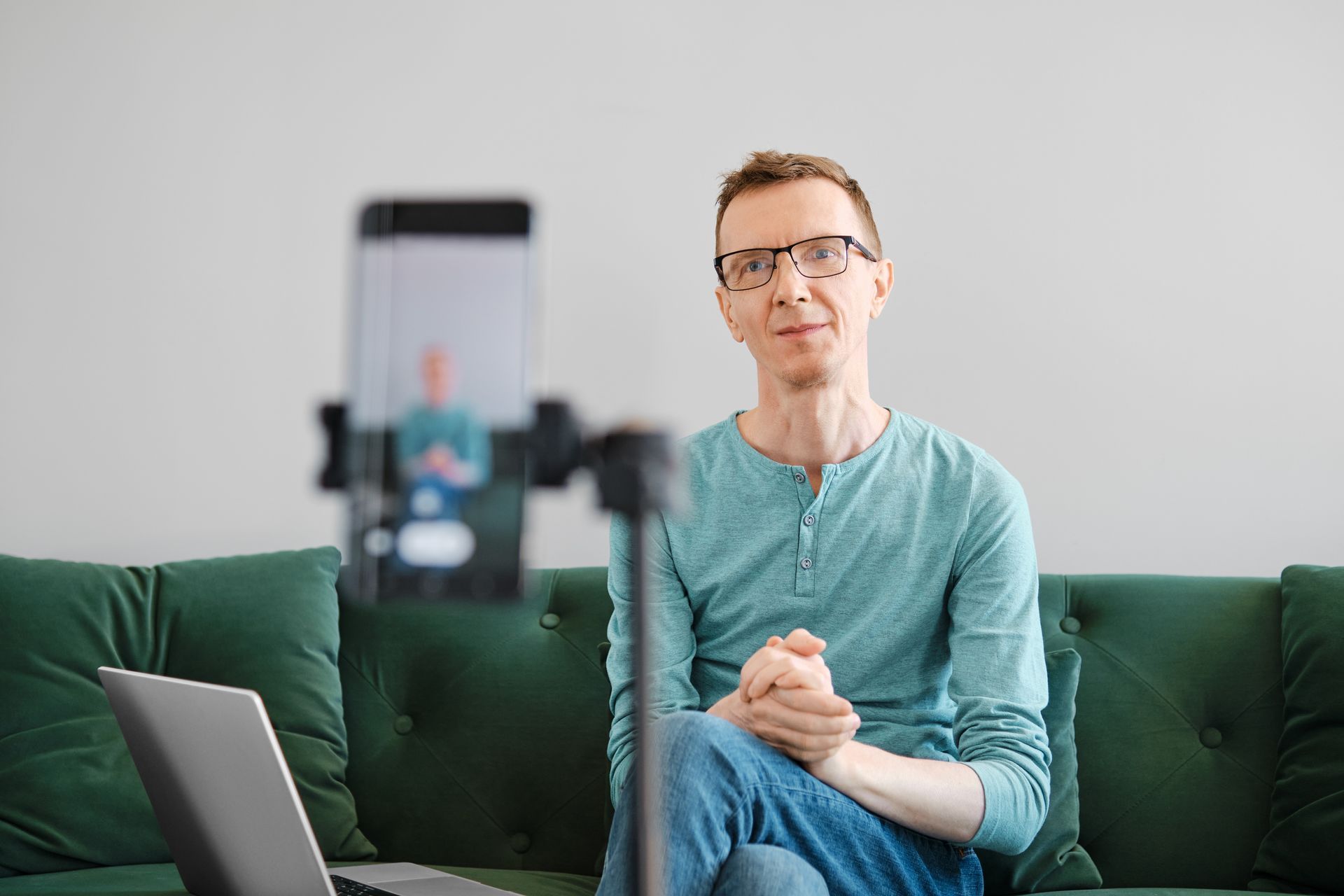 A man is sitting on a couch in front of a laptop and a cell phone.