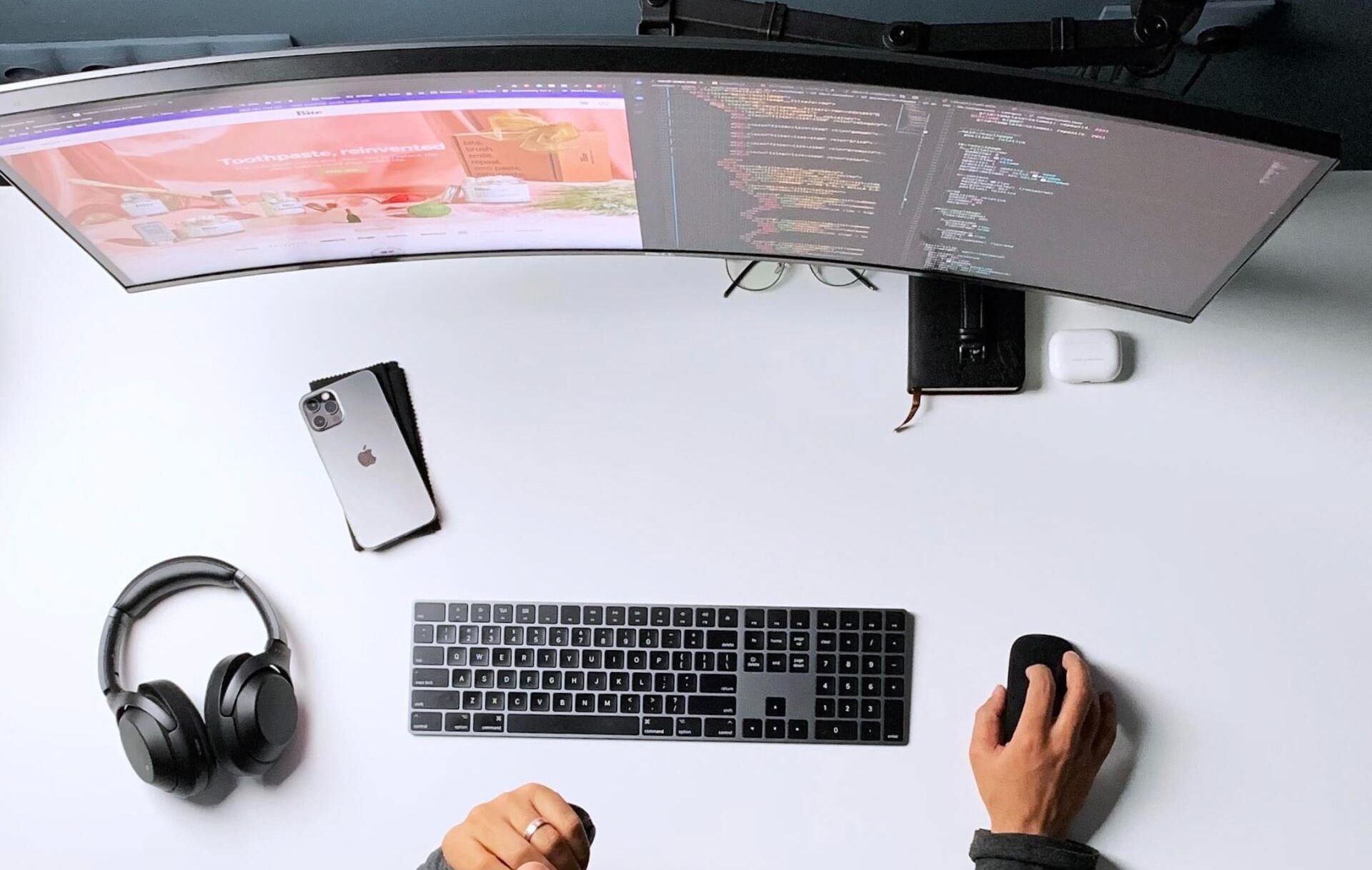 A person is sitting at a desk with a computer , keyboard , mouse and headphones.