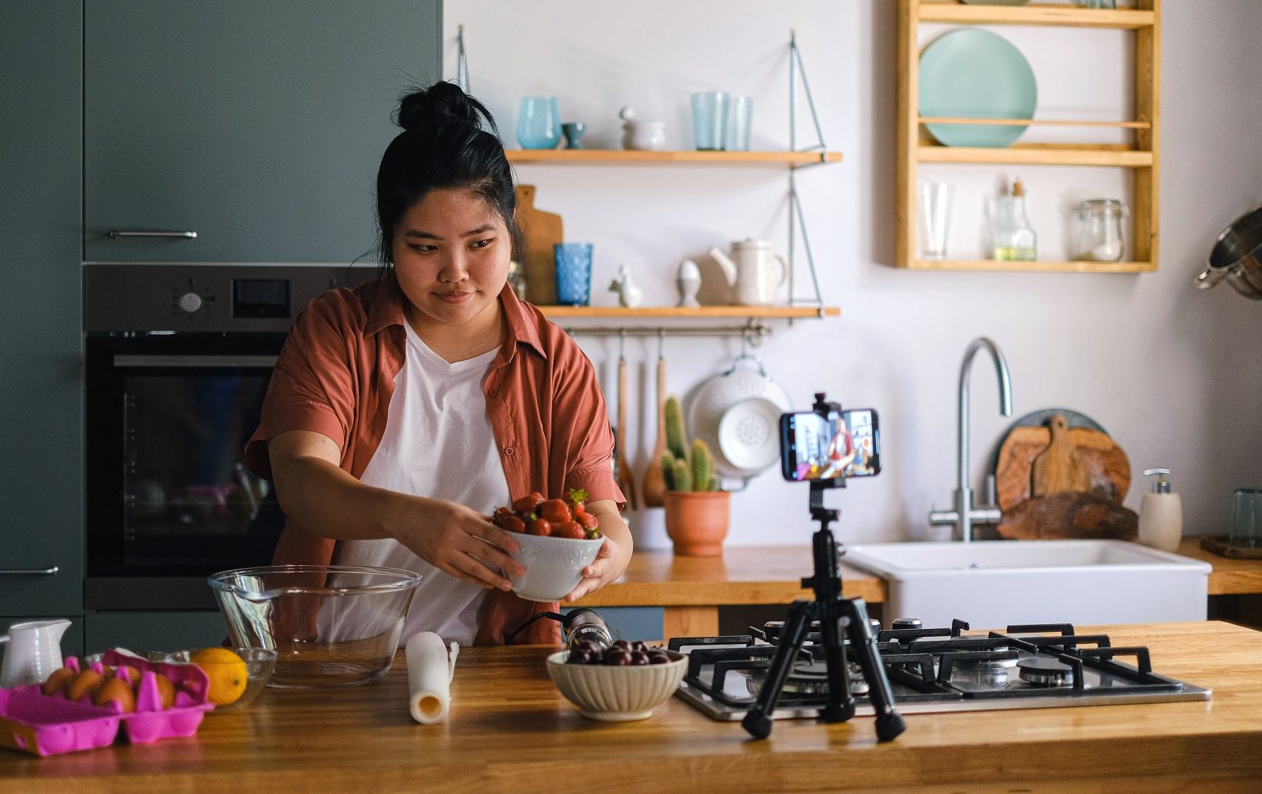 A woman is making a video of herself cooking in a kitchen.