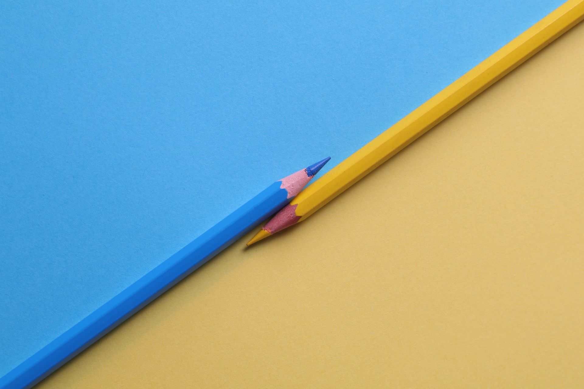 A blue pencil and a yellow pencil are on a blue and yellow background.