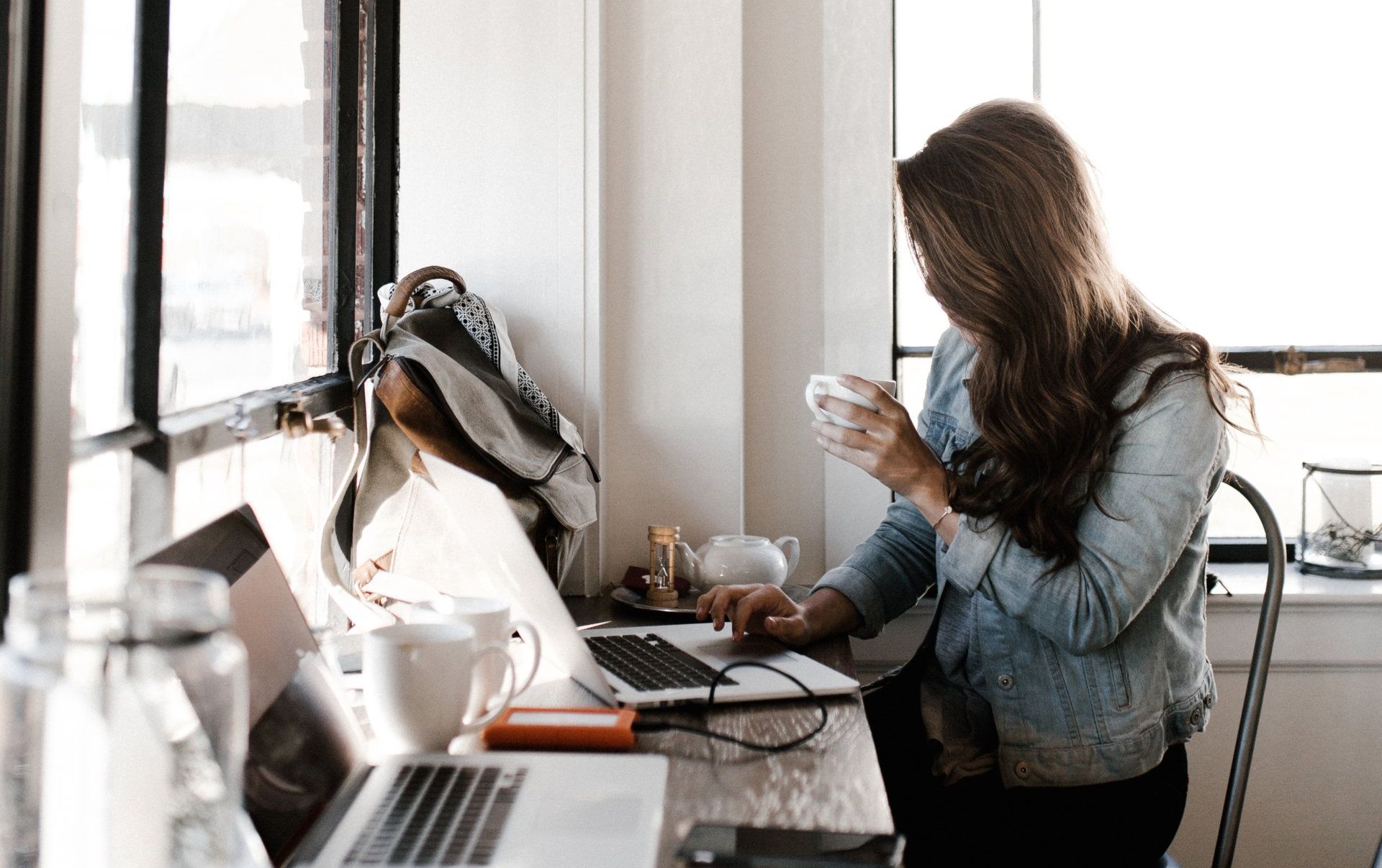 A woman is sitting at a table with a laptop and a cup of coffee.