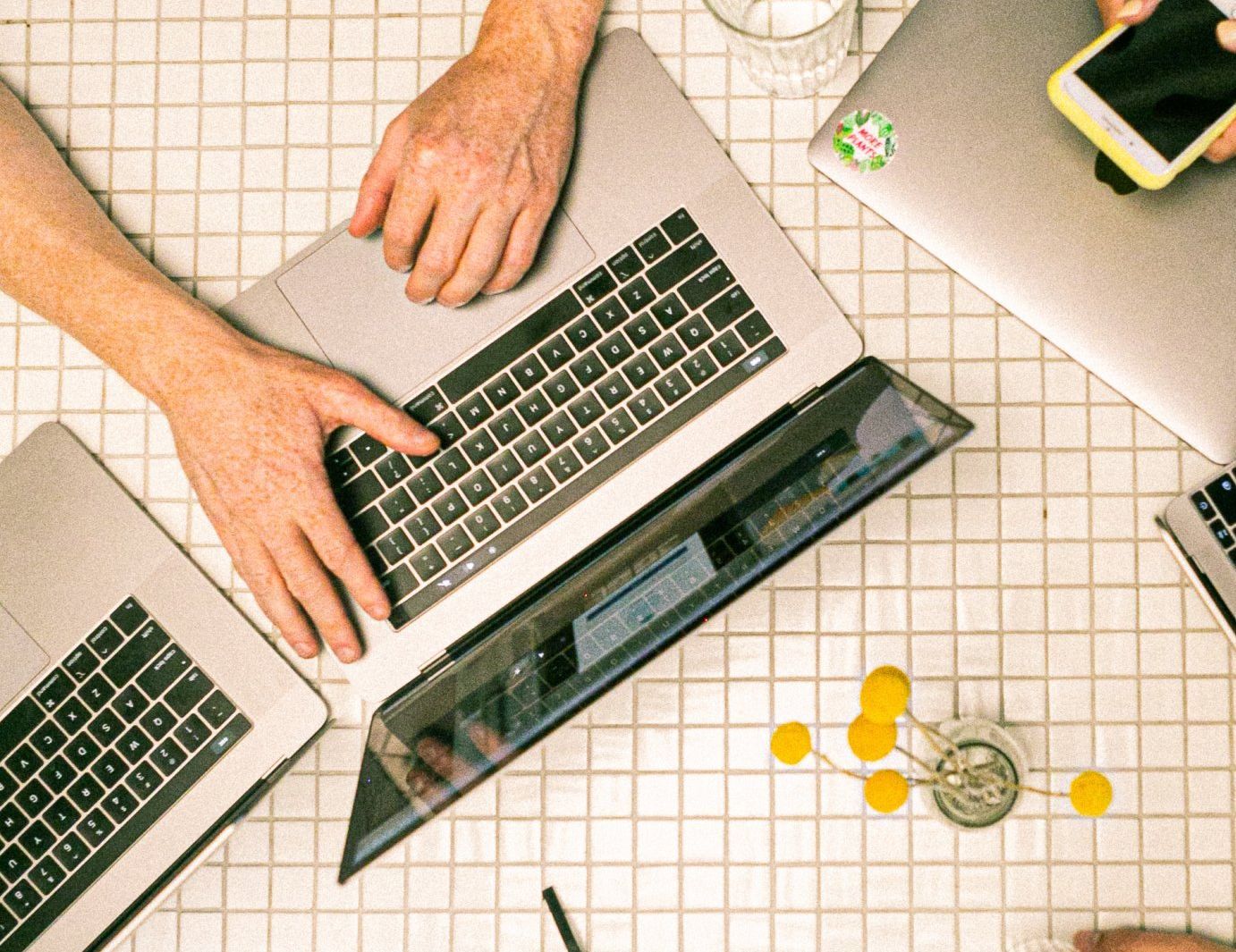 A group of people are working on laptops on a tiled table.