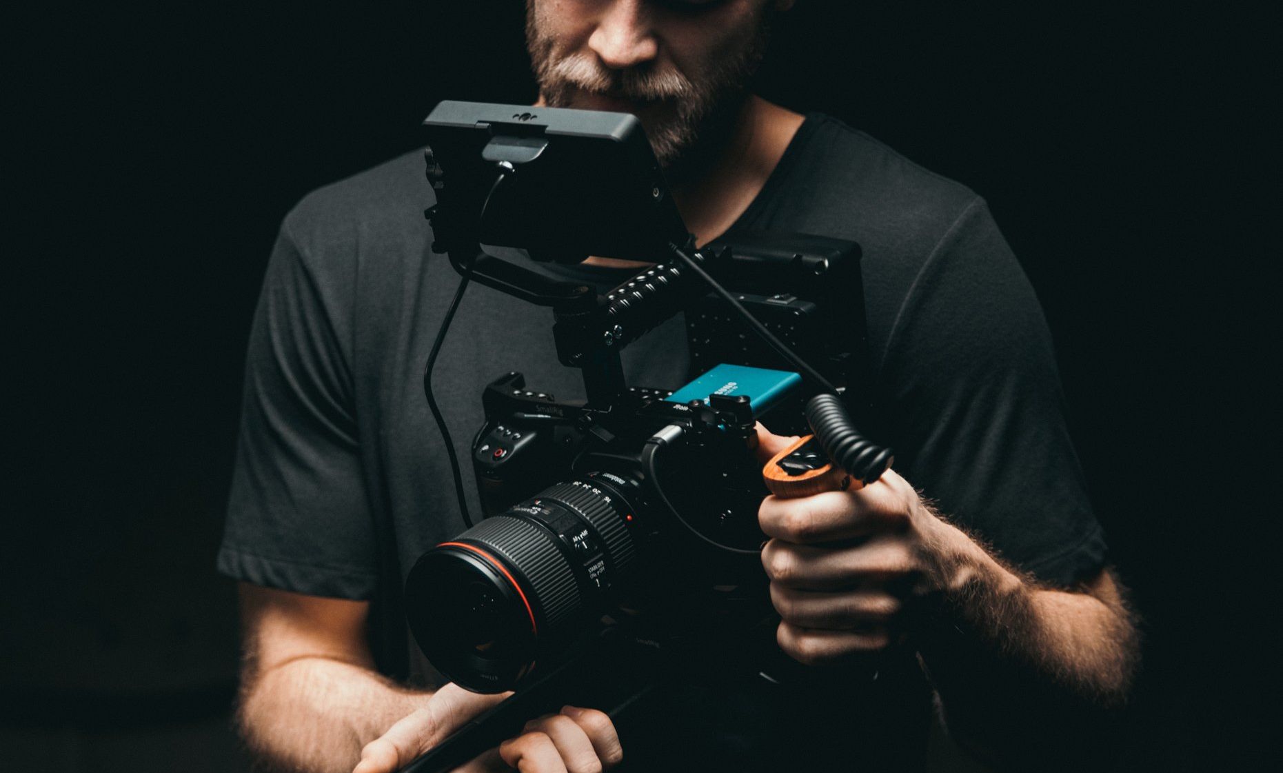 A man is holding a camera in his hands in a dark room.