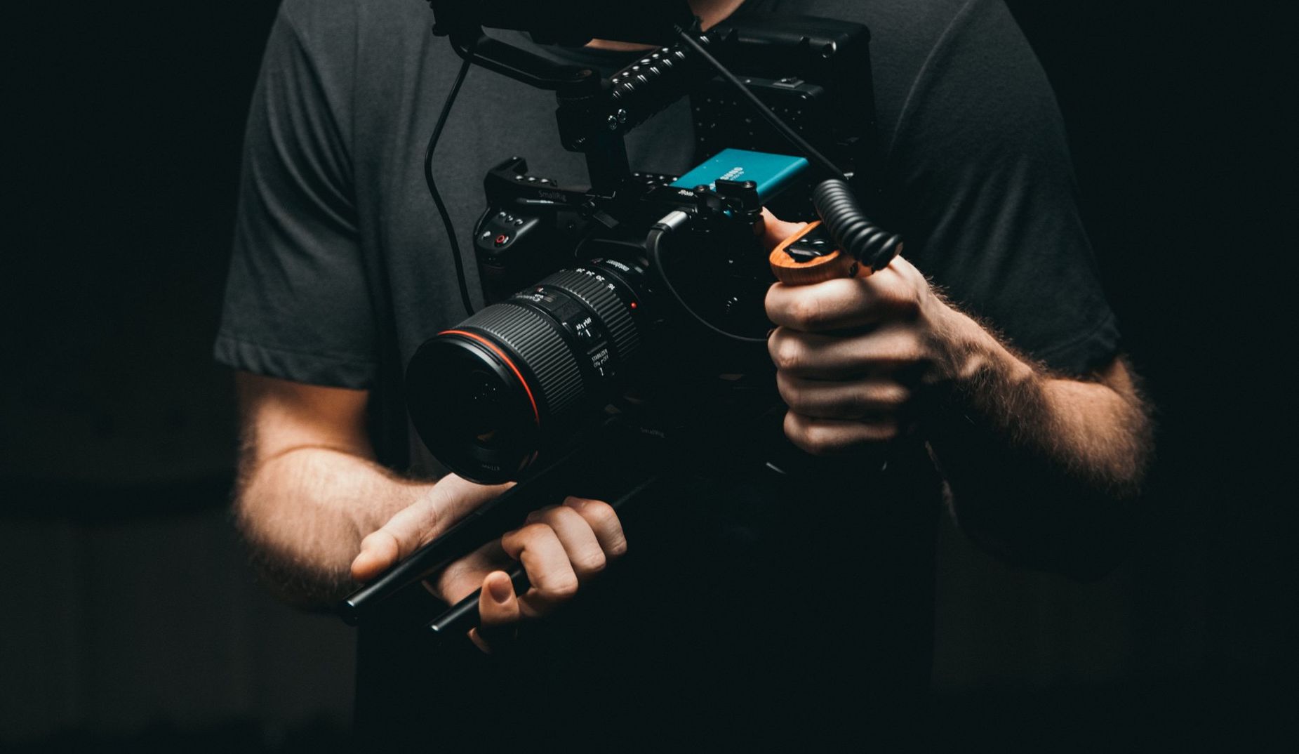 A man is holding a camera in his hands in a dark room.