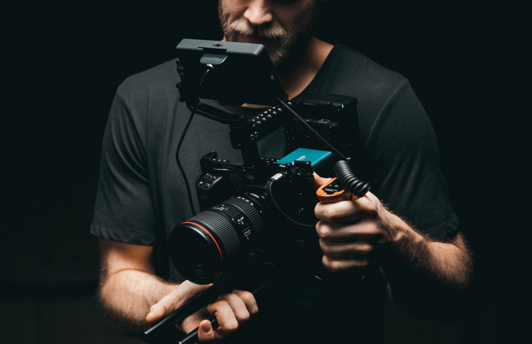 A man is holding a camera in his hands in a dark room.