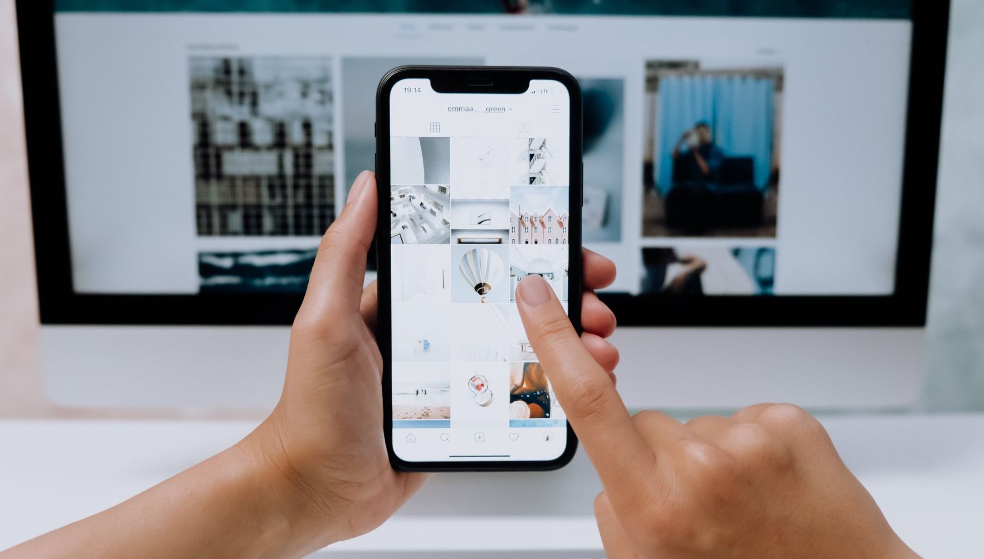 A person is holding a cell phone in front of a computer screen.