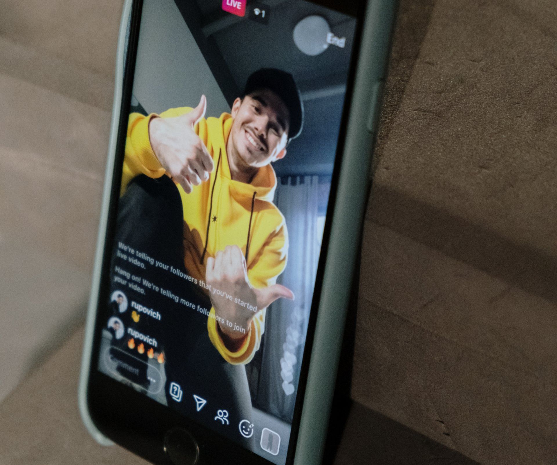 A man in a yellow hoodie is giving a thumbs up on a cell phone