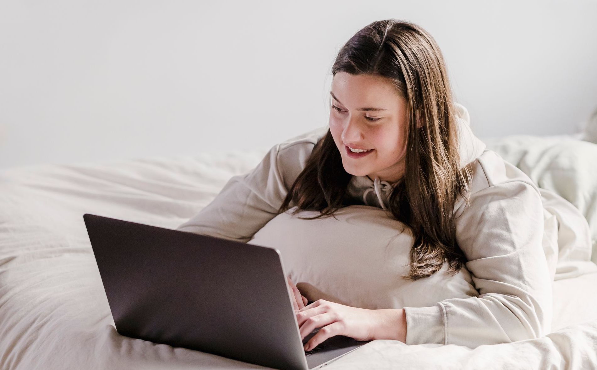 A woman is laying on a bed using a laptop computer.