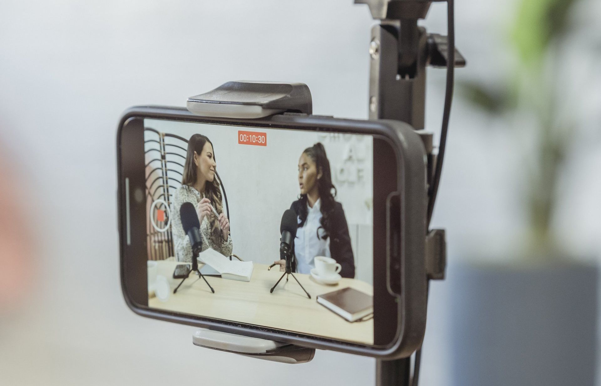 A cell phone is being used to record a video of two women talking into microphones.