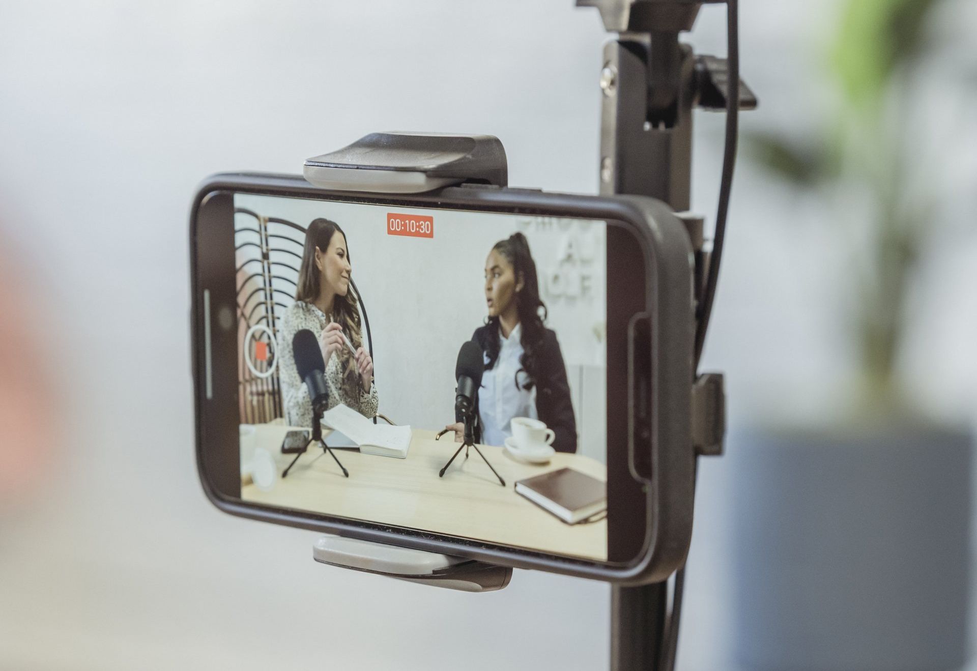 A cell phone is being used to record a video of two women talking into microphones.