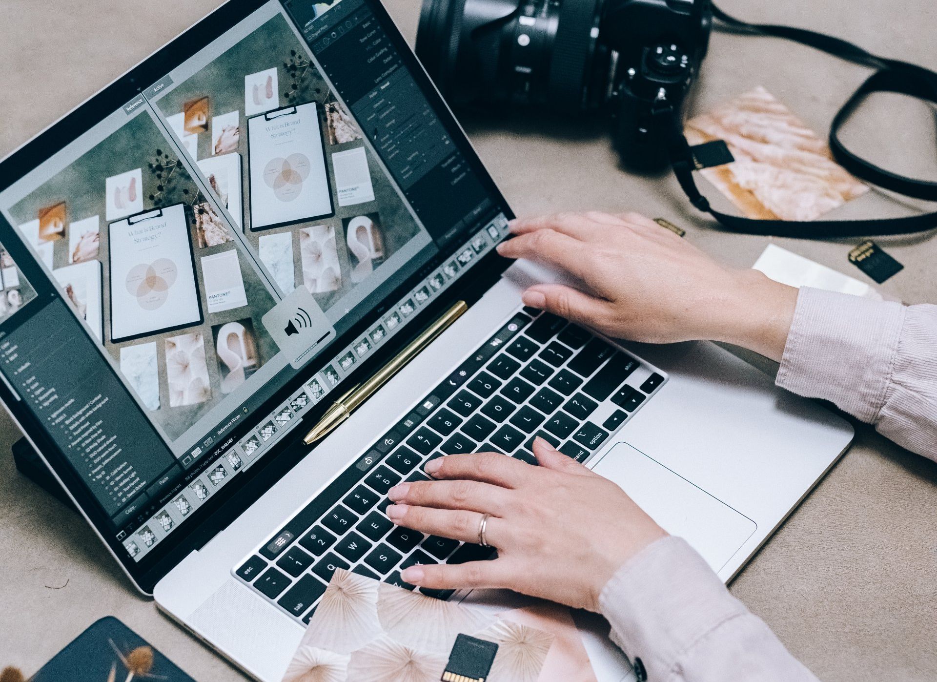 A person is typing on a laptop computer next to a camera.