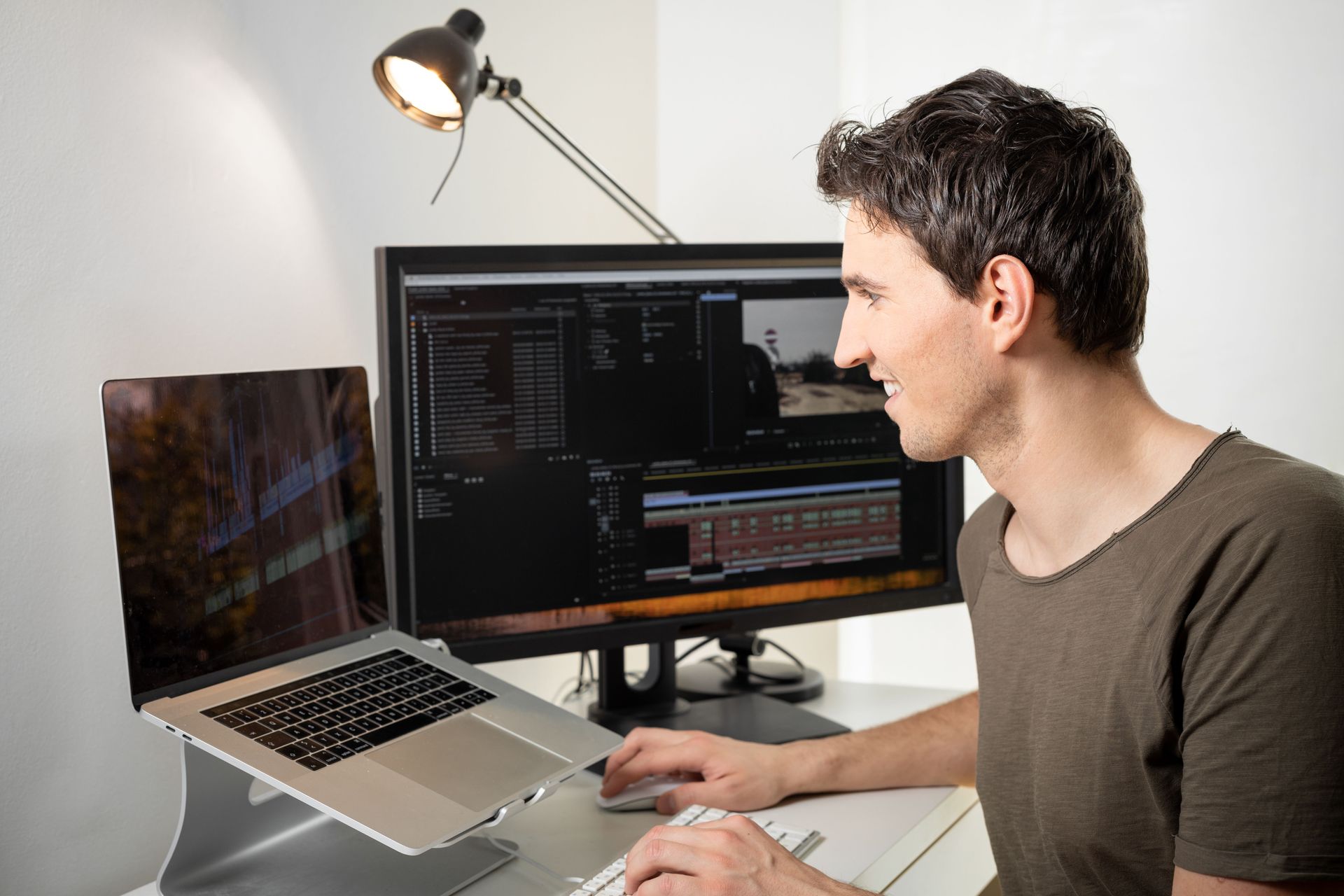 A man is sitting at a desk using a laptop computer and a monitor.