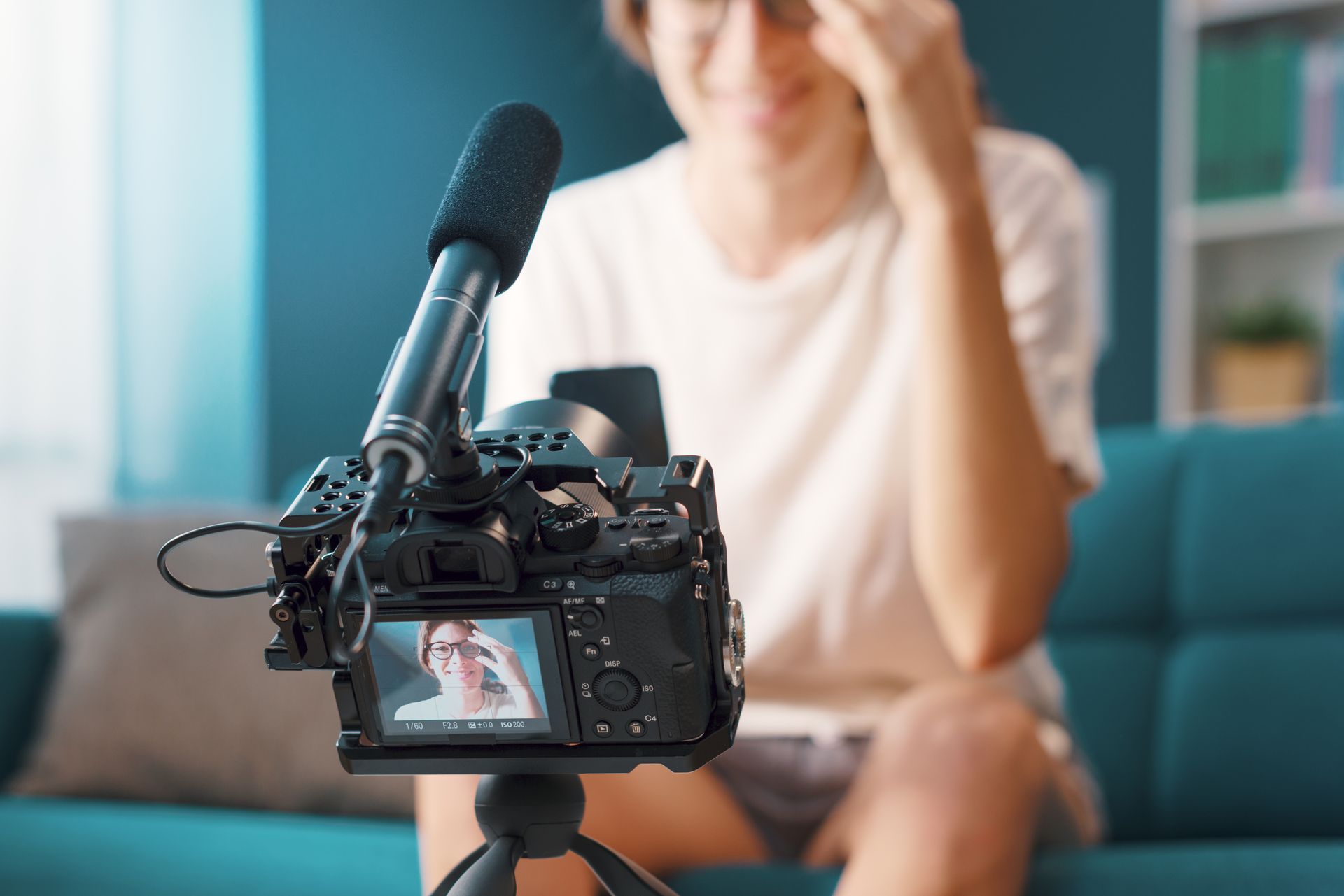 A woman is sitting on a couch being filmed by a camera.