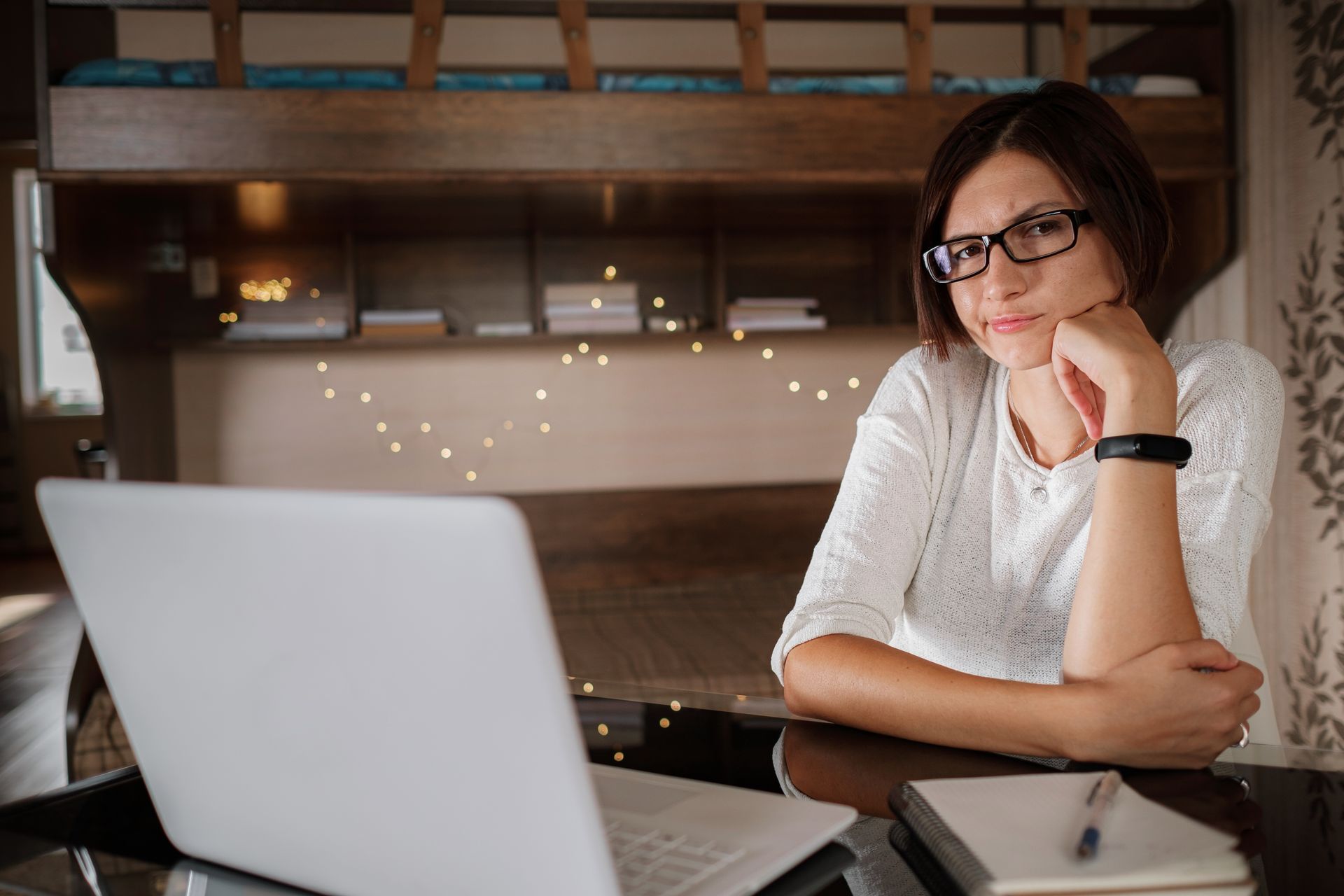 A woman wearing glasses is sitting at a desk in front of a laptop computer.
