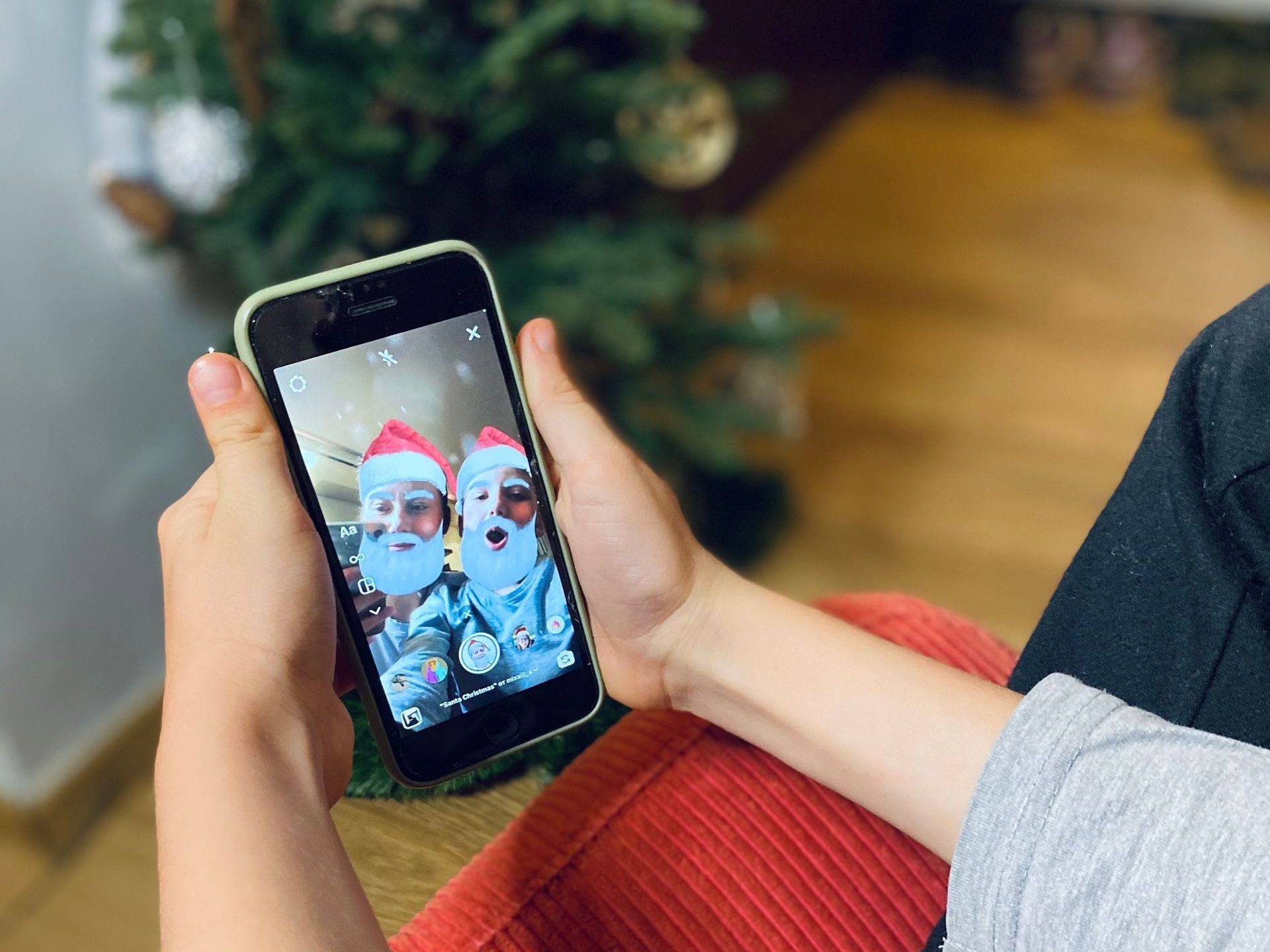 A person is holding a cell phone in front of a christmas tree.