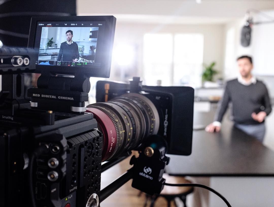 Camera filming a man in a kitchen; camera and screen in the foreground, man at a counter in the background.
