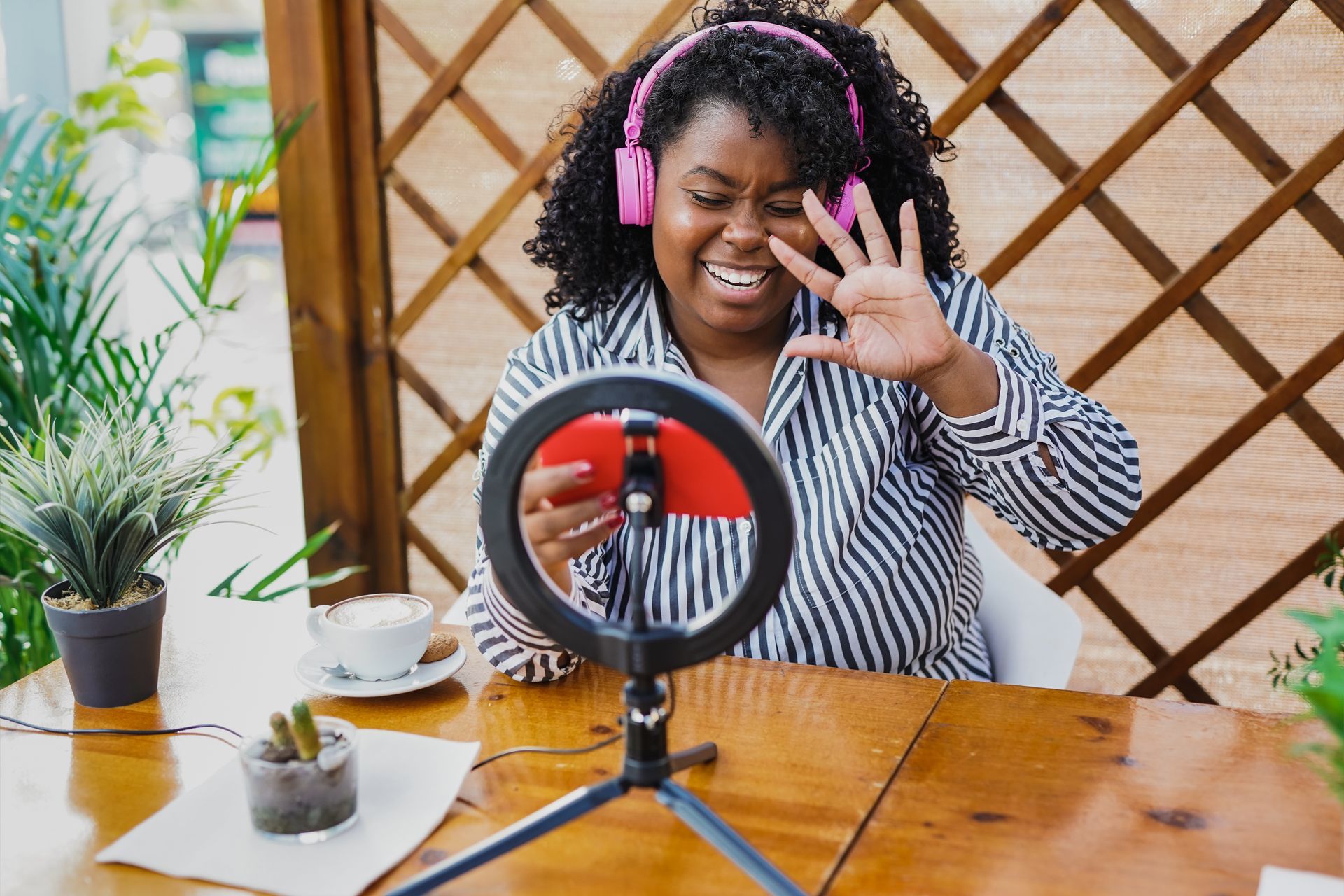 A woman wearing headphones is sitting at a table taking a selfie with a ring light.