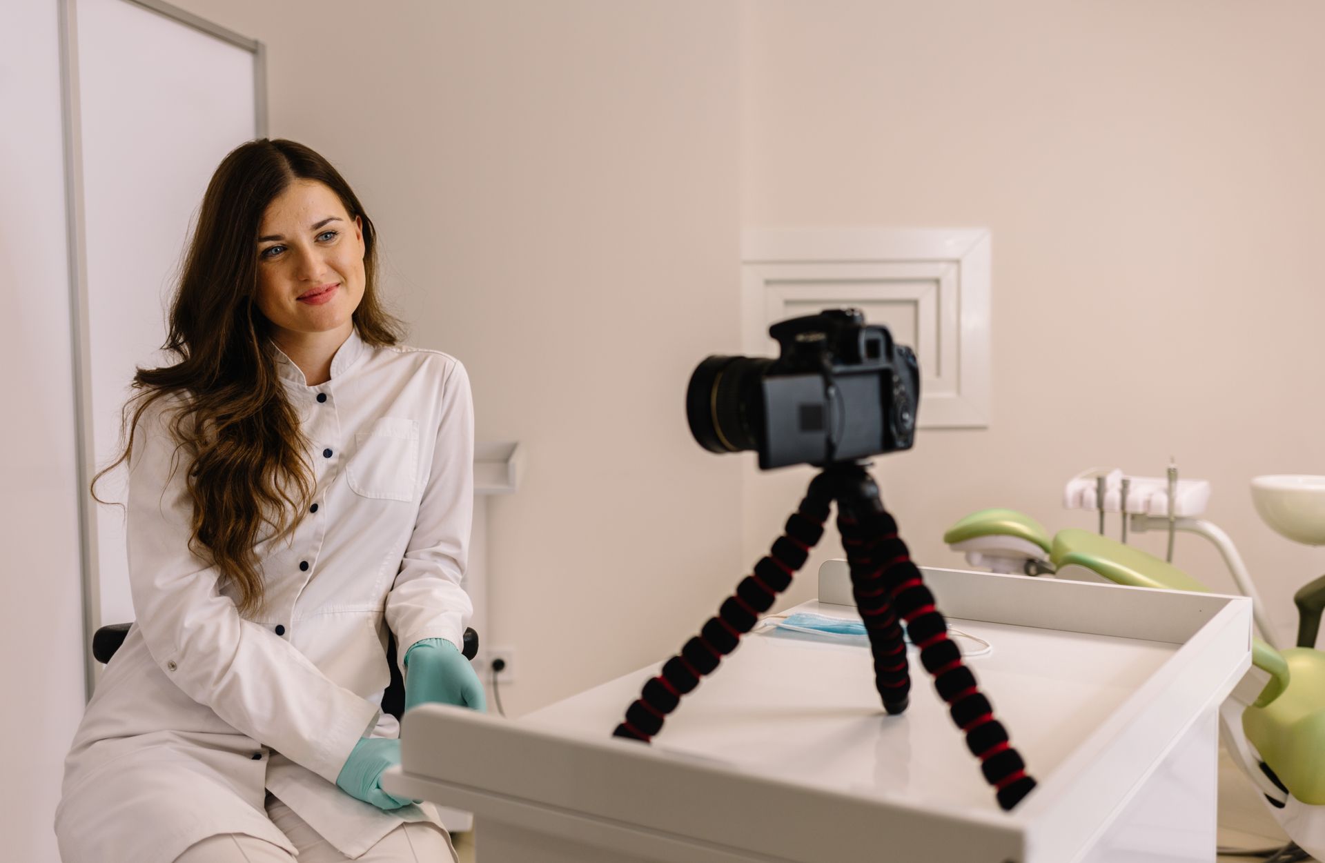 A female dentist is sitting in front of a camera on a tripod.