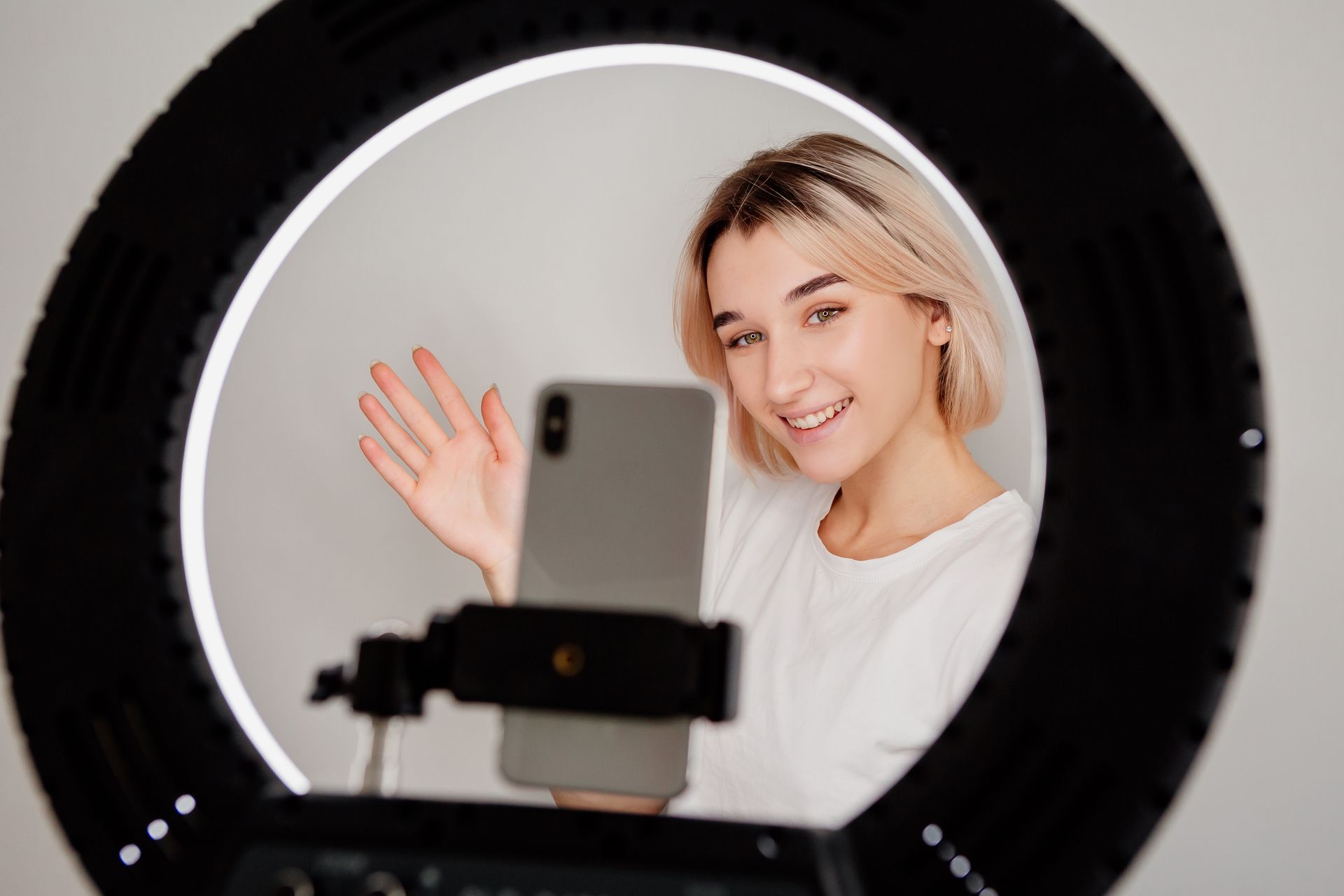 A woman is taking a selfie with her phone in front of a ring light.