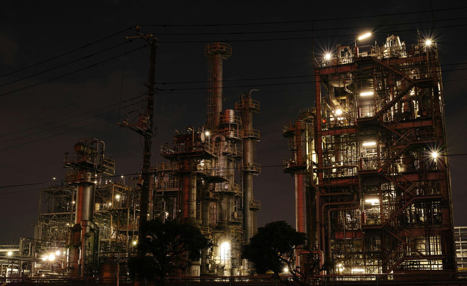 Night view of an industrial complex lit by numerous lights, with tall structures and chimneys against a dark sky.