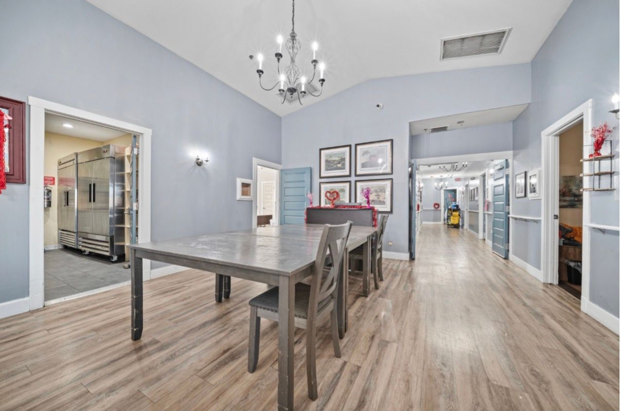 Bright dining room with blue walls, wood floor, chandelier, table, chairs, and office doorway.