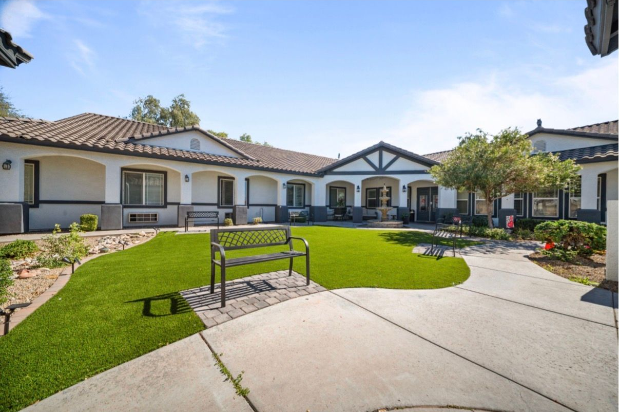 Courtyard with a manicured lawn, curved walkway, bench, and single-story homes under a blue sky