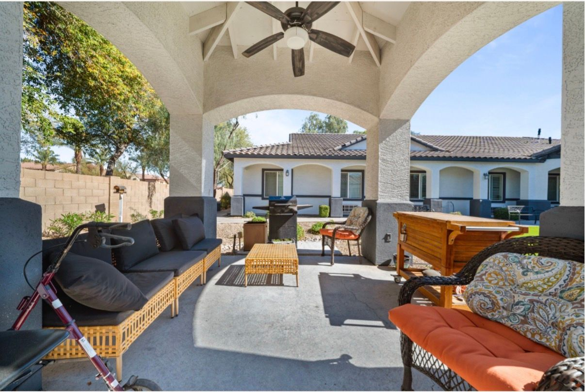Covered patio with outdoor seating, ceiling fans, and a view of a house and yard.