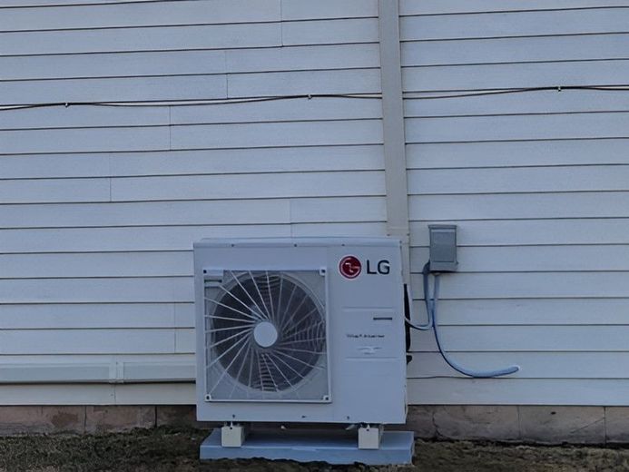 LG outdoor air conditioner unit beside a white house wall and windowless siding.