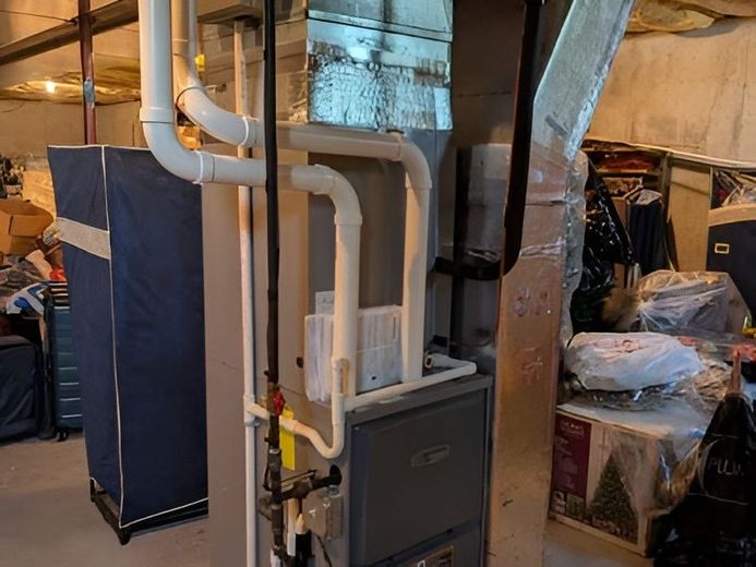 Basement utility area with a furnace, white PVC pipes, and ductwork beside storage items.