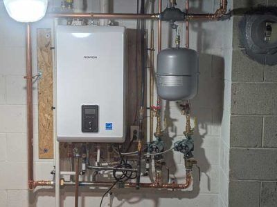 Wall-mounted boiler and plumbing system in a utility room, with gray expansion tank and copper pipes.