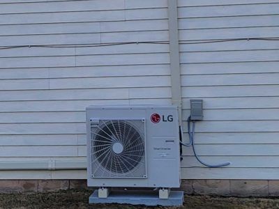 LG outdoor air conditioner unit beside a white house wall with blue conduit piping.