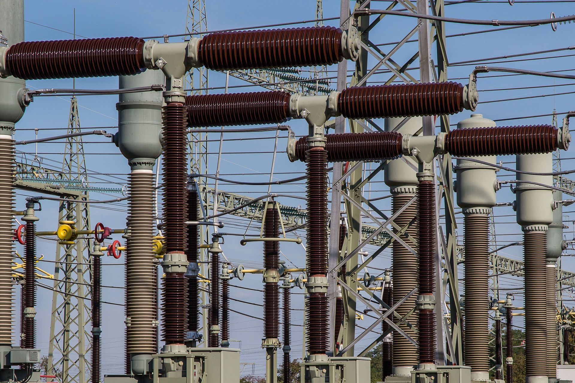 Electrical substation with rows of tall gray insulators and rust-colored power lines under a blue sky
