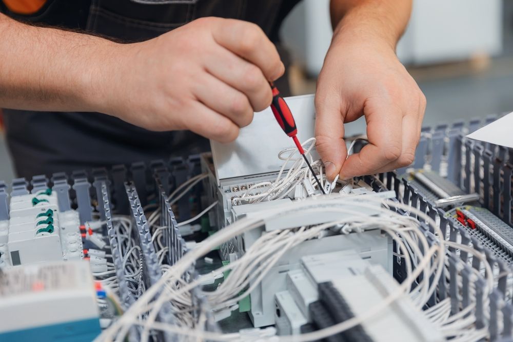 Technician testing network wiring in a server rack with red screwdriver and white cables