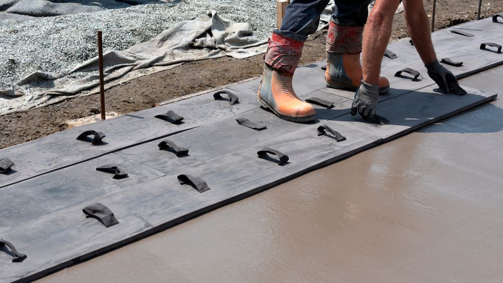 Workers applying concrete stamping mats on wet concrete surface to create decorative patterns during