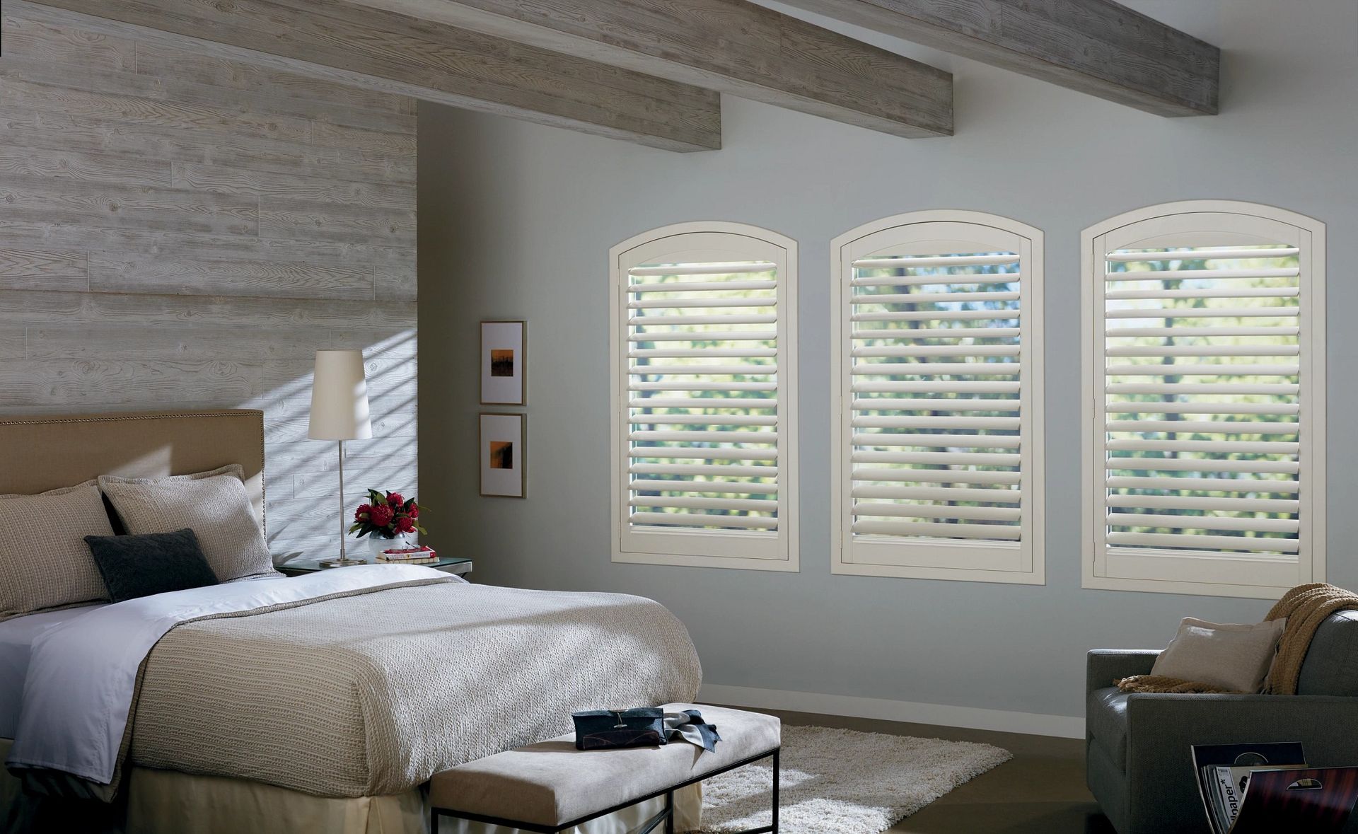 Bedroom with bed, three arched windows with shutters, sofa, and bench.