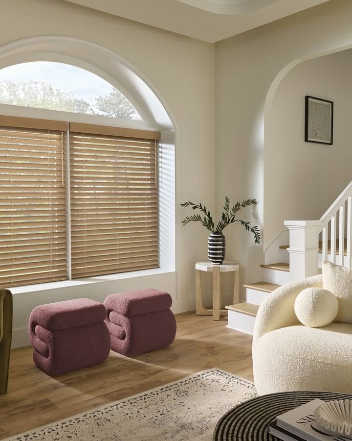 Living room with arched window, wooden blinds, seating, and a decorative vase.