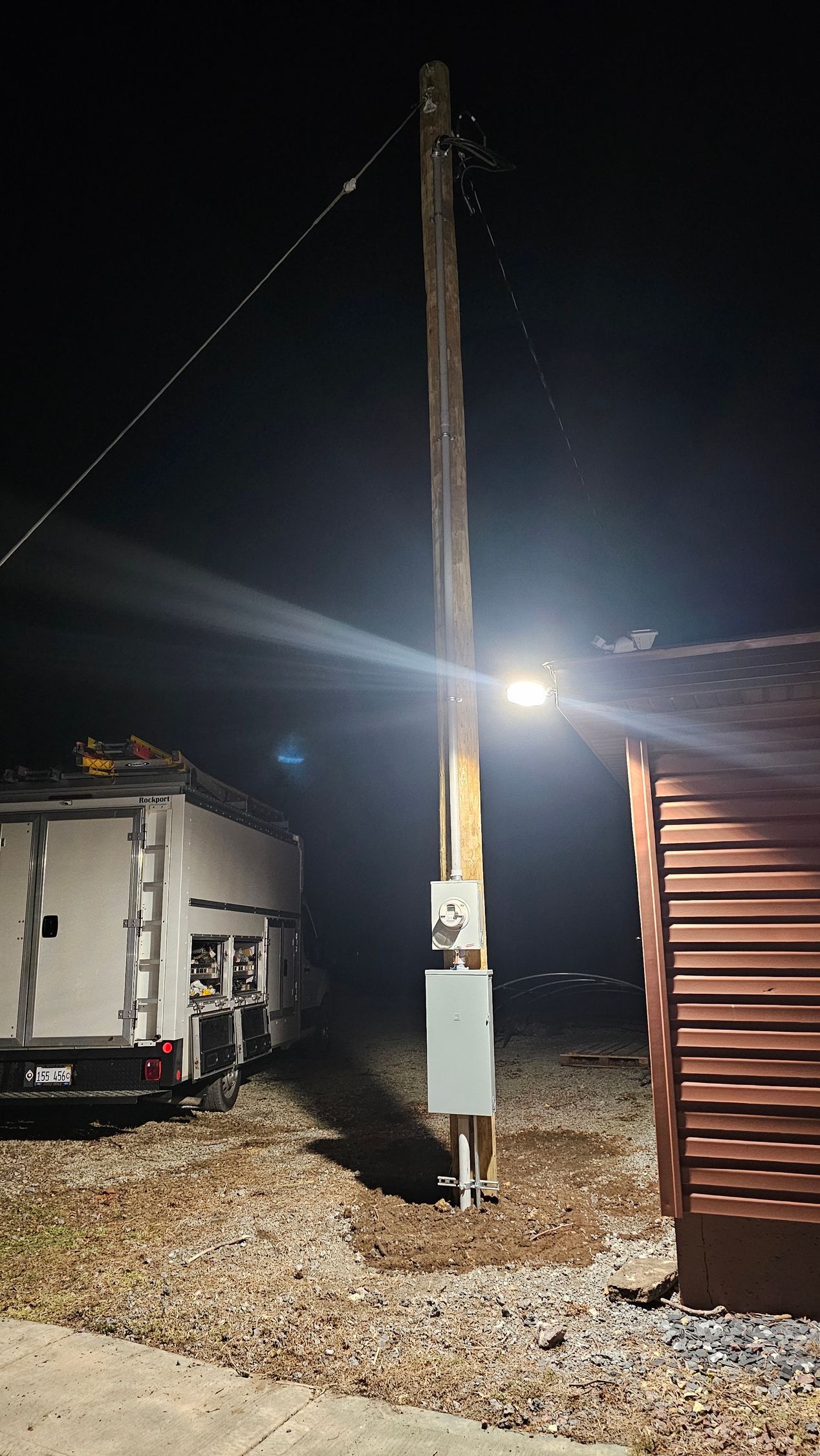 A telephone pole with a light on it is lit up at night.