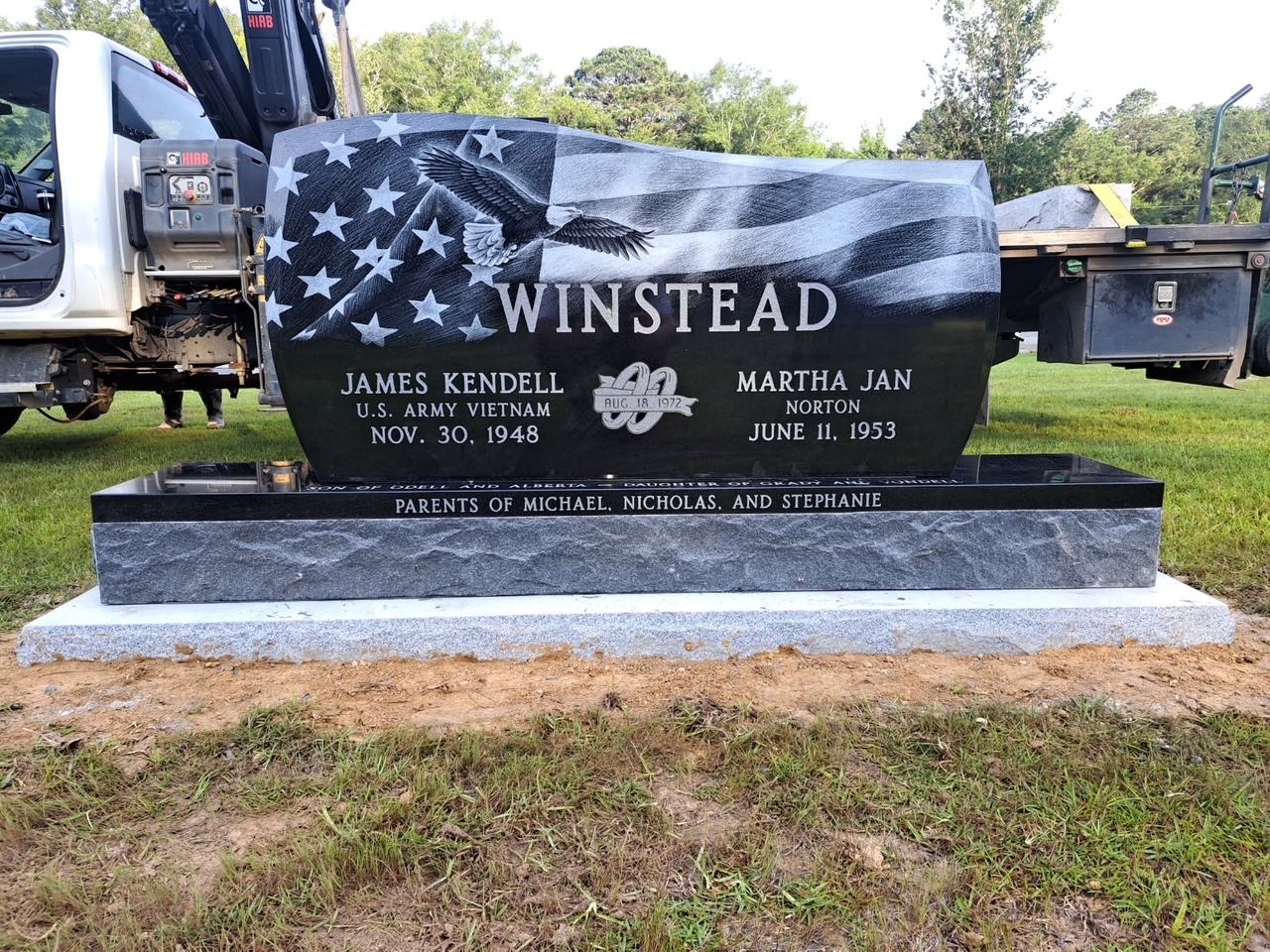 A black polished granite tombstone for the Winstead family, featuring an engraved American flag, set on a grass lawn.