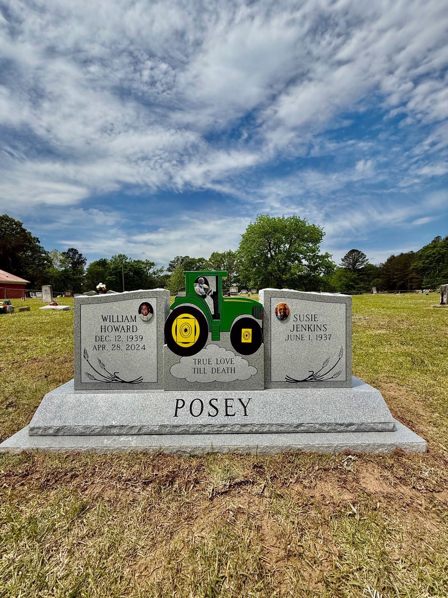 A grey granite headstone in a cemetery with a green tractor emblem and the name