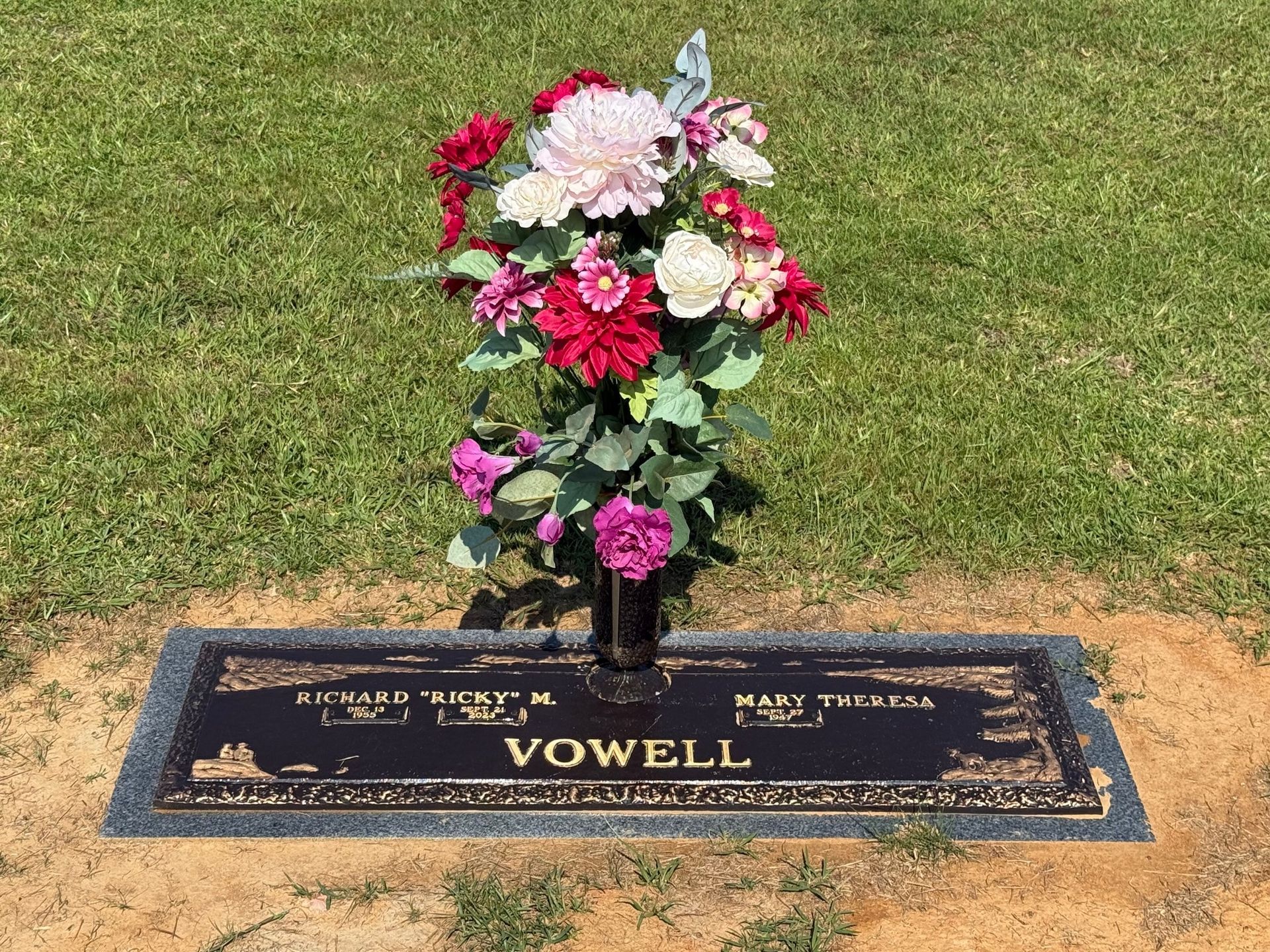 A bronze burial marker for the Vowell family, featuring a vibrant floral bouquet, set in a grassy cemetery lawn.