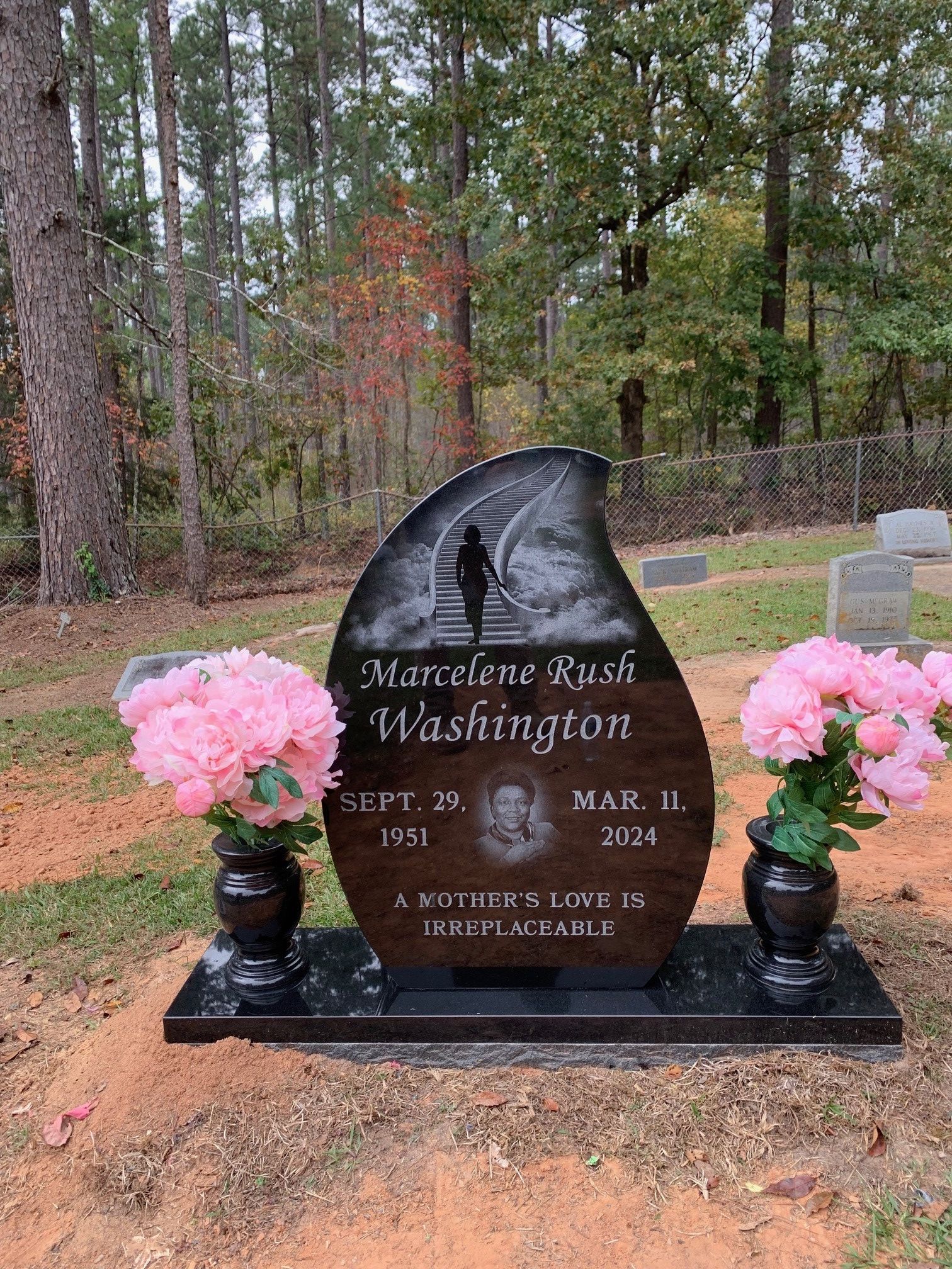 A teardrop-shaped black headstone for Marcelene Rush Washington with an engraving of a staircase and two vases of flowers.