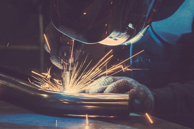 Welder in Protective Gear Welding a Metal Pipe, Creating Sparks — Mid City Smash Repairs in Dubbo, NSW