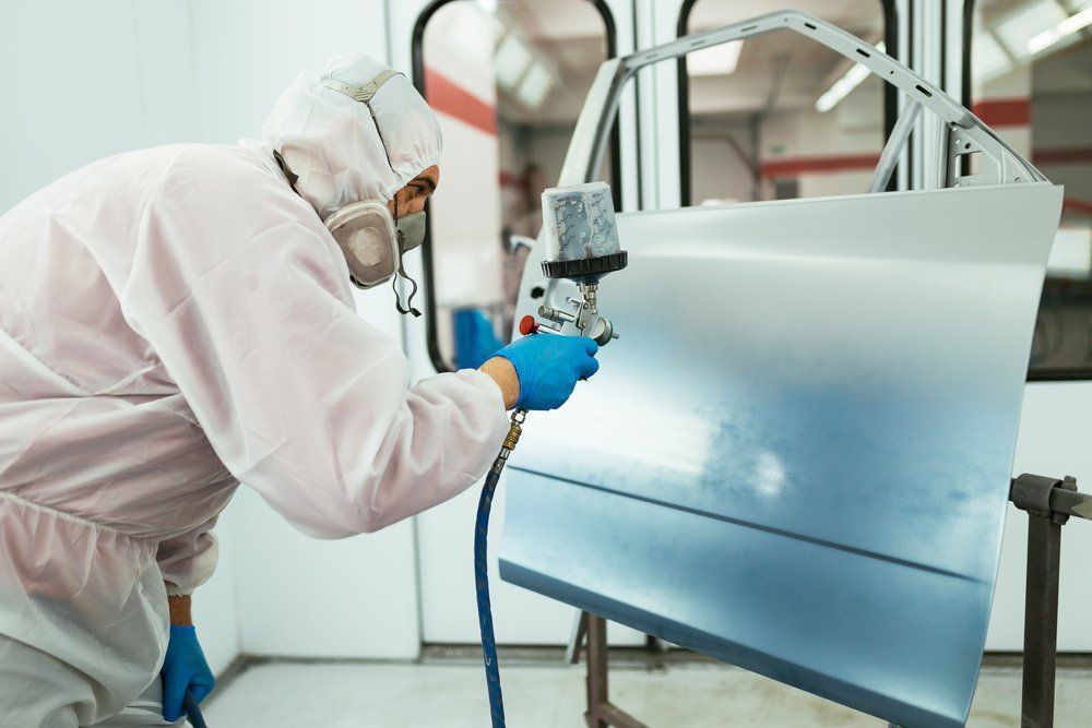 Person in Protective Suit Spraying Paint on a Car Door in a Body Shop — Mid City Smash Repairs in Dubbo, NSW