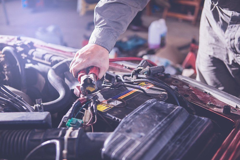 Mechanic Working on Car Engine, Using Tool on the Battery in a Garage Setting — Mid City Smash Repairs in Dubbo, NSW