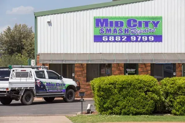 Mid City Smash Repairs building and service truck, green and blue logo sign, brick facade.