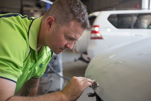 Man in Green Shirt Inspecting White Car for Damage — Mid City Smash Repairs in Dubbo, NSW