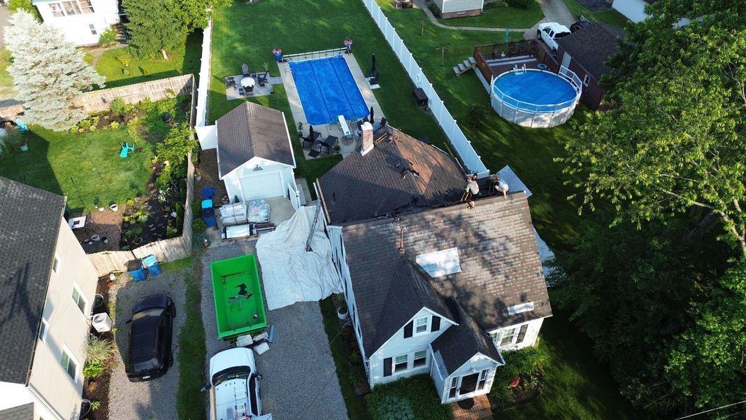 Overhead view of a house with a pool, covered in blue tarp. Roofers are working on the roof.