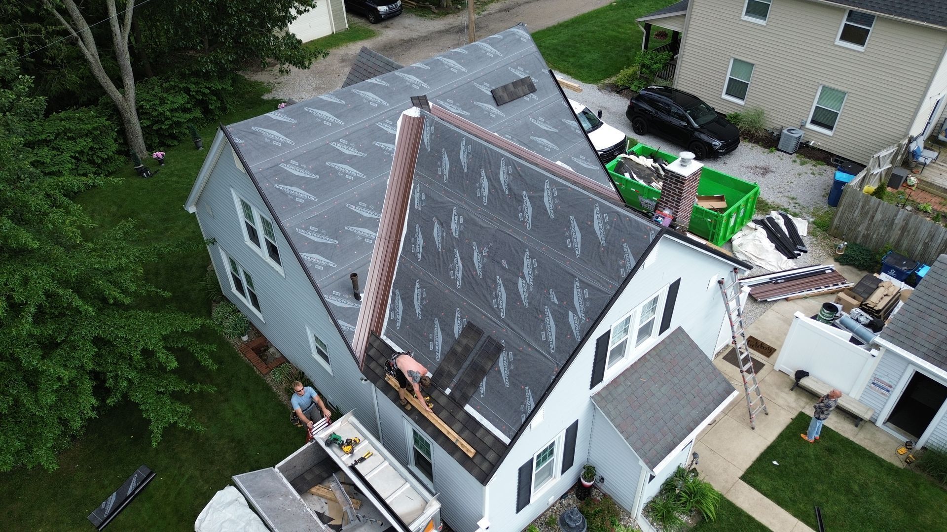 House with roof partially replaced, construction in progress; workers visible.