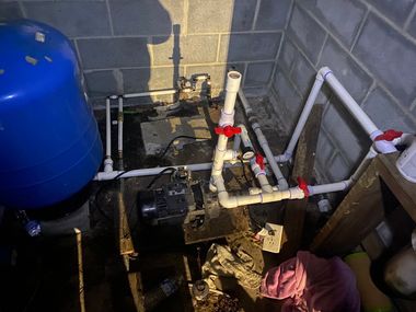 Basement water system with blue tank, black pump, and white PVC pipes connected to a gray wall