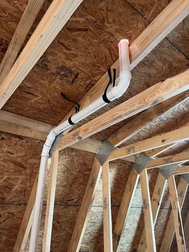Insulated white pipe runs along unfinished wooden rafters in an attic framing space